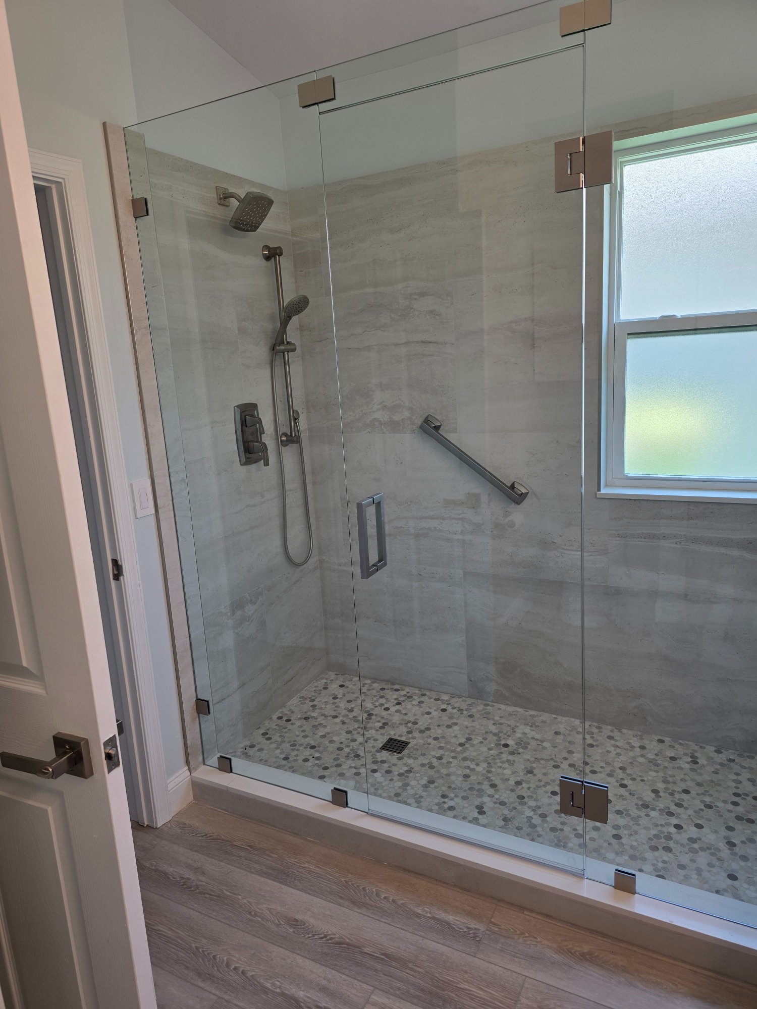 Master bathroom after — frameless glass shower enclosure, full-length wall, brushed nickel hardware, bench seat, penny tile floor